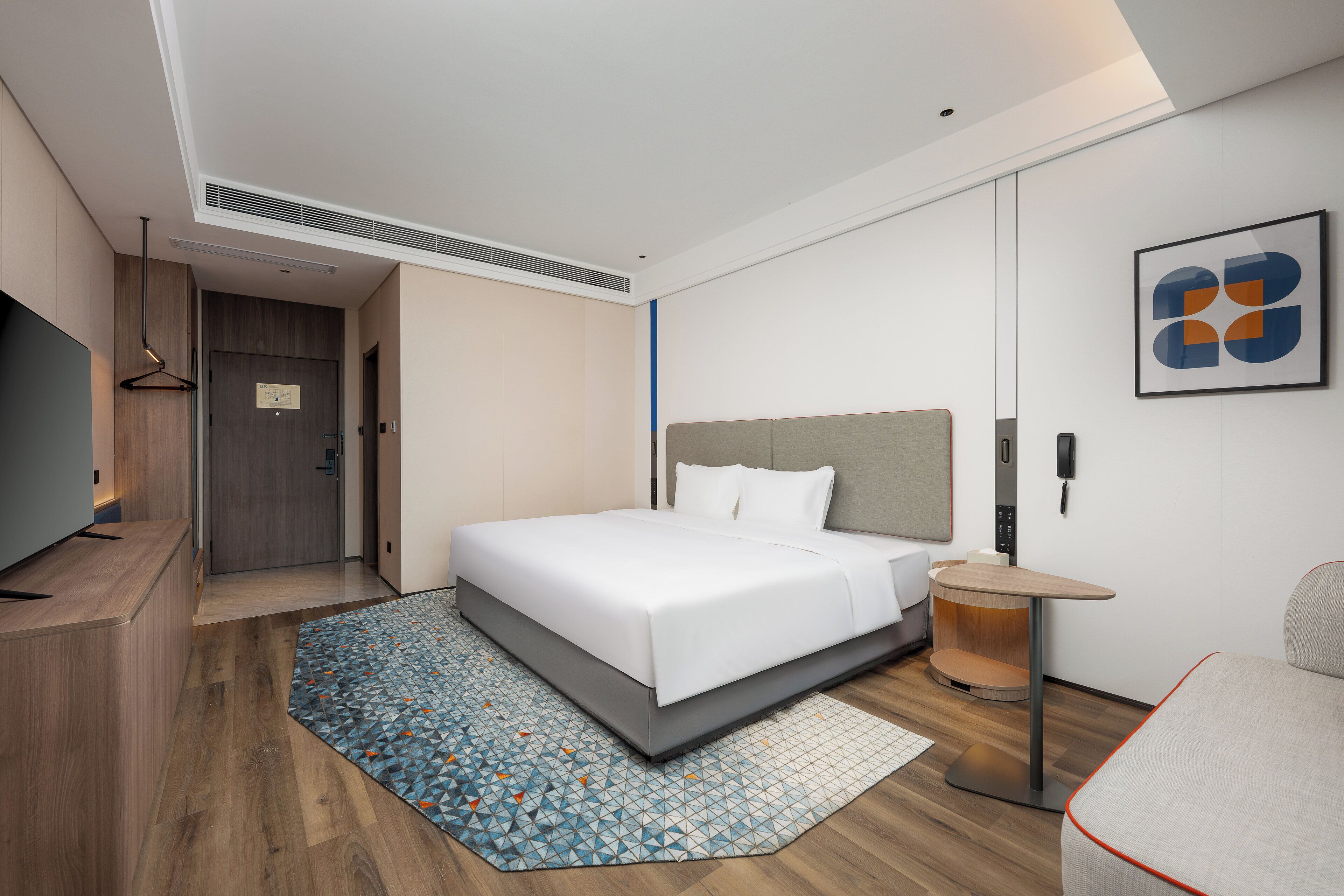 A modern hotel room with a large bed, a desk, a chair, and a small table.