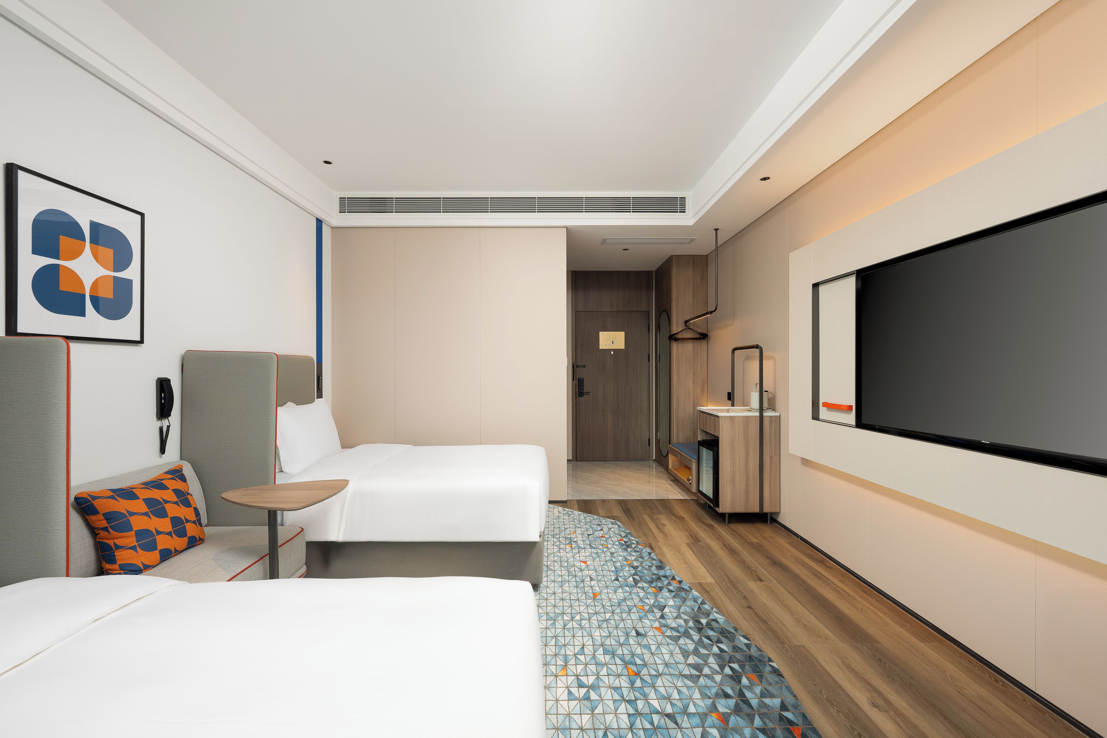 A modern hotel room with two beds, a TV, a desk, and a bathroom visible through an open door.