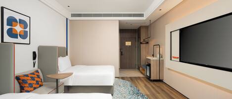 A modern hotel room with two beds, a TV, a desk, and a bathroom visible through an open door.