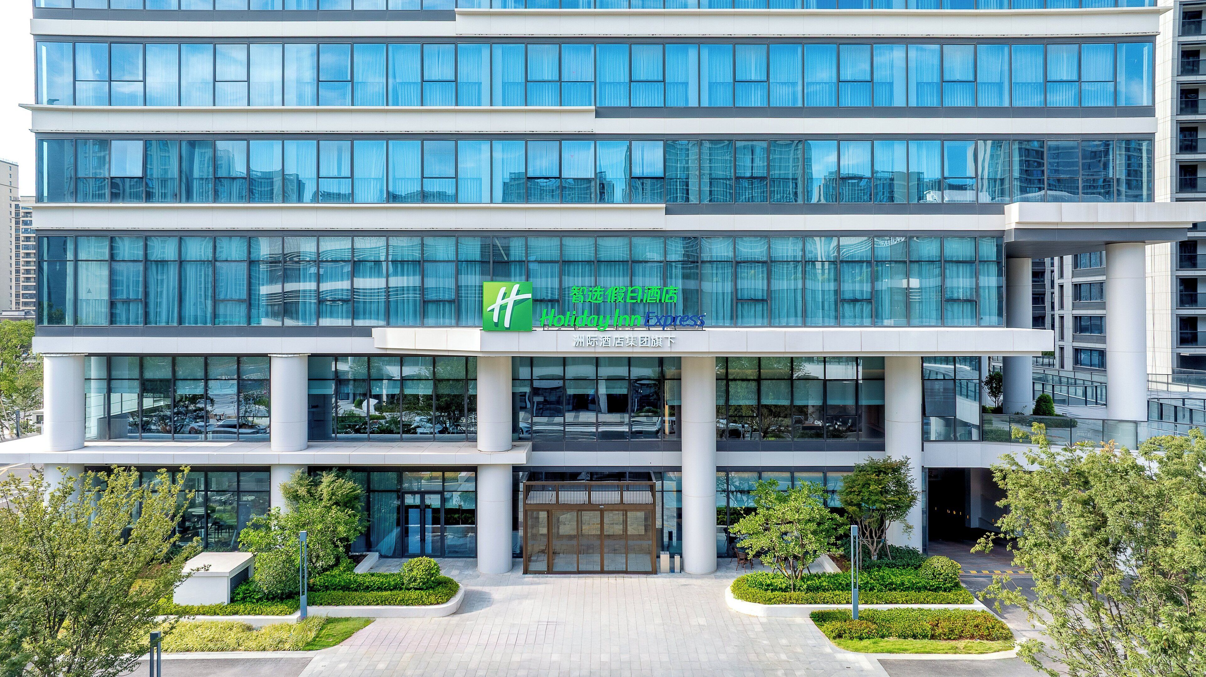 Ein modernes Hotelgebäude mit Glasfassade, einem grünen Logo und einem Schild für Holiday Inn Express.