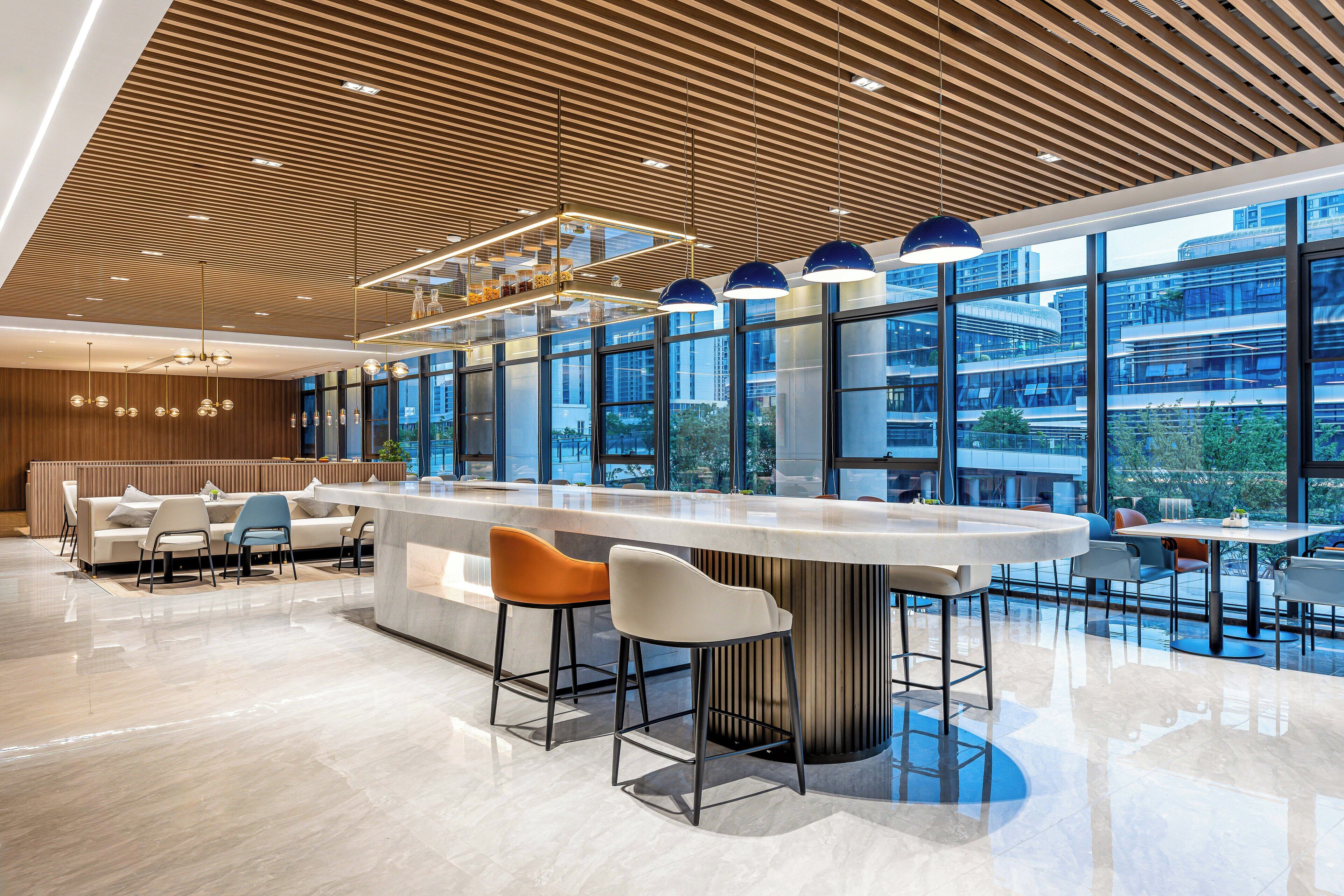 A modern bar area with a curved counter, two bar stools, and a seating area with a sofa and chairs.