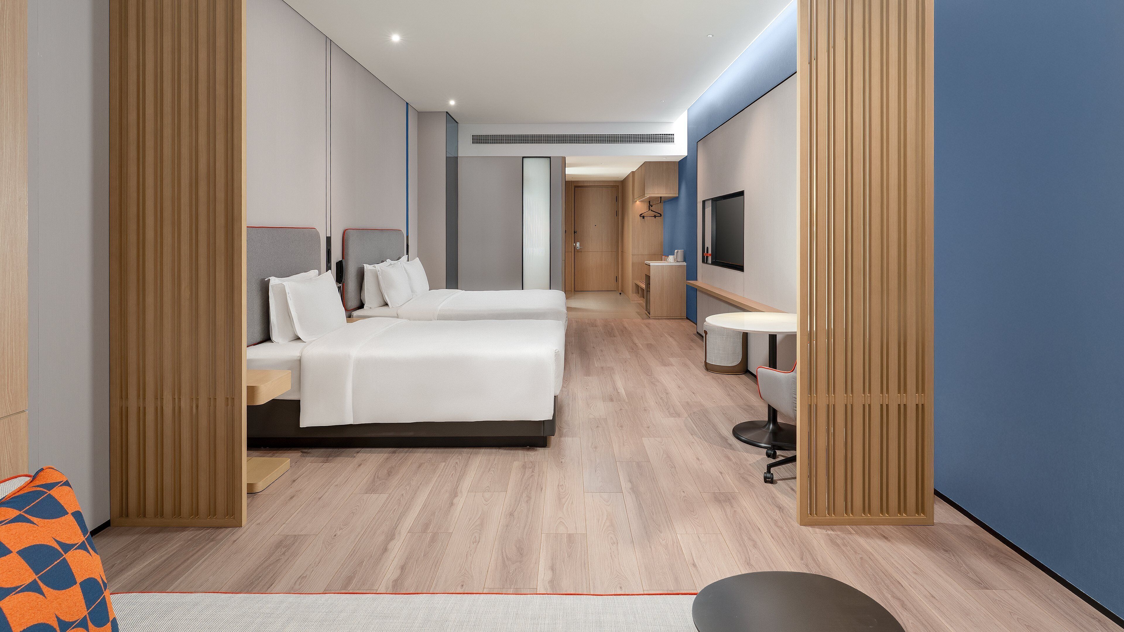 Ein modernes Hotelzimmer mit zwei Betten, einem Fernseher und einer kleinen Essecke.