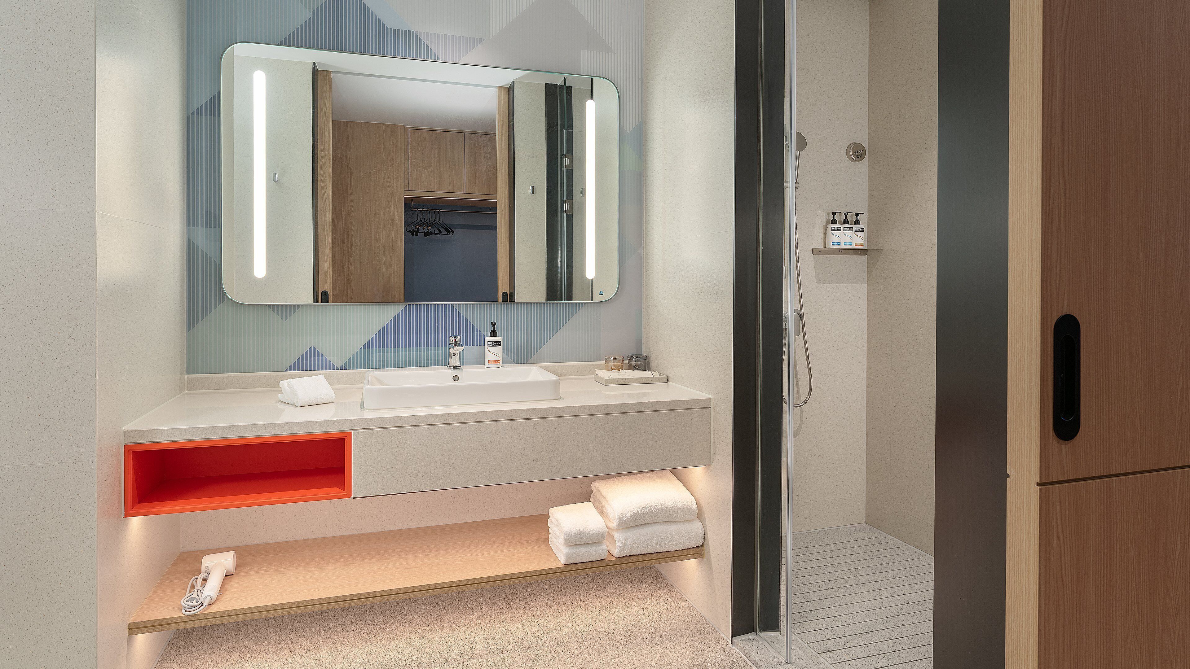 A modern bathroom with a large mirror, a sink, and a shower area.