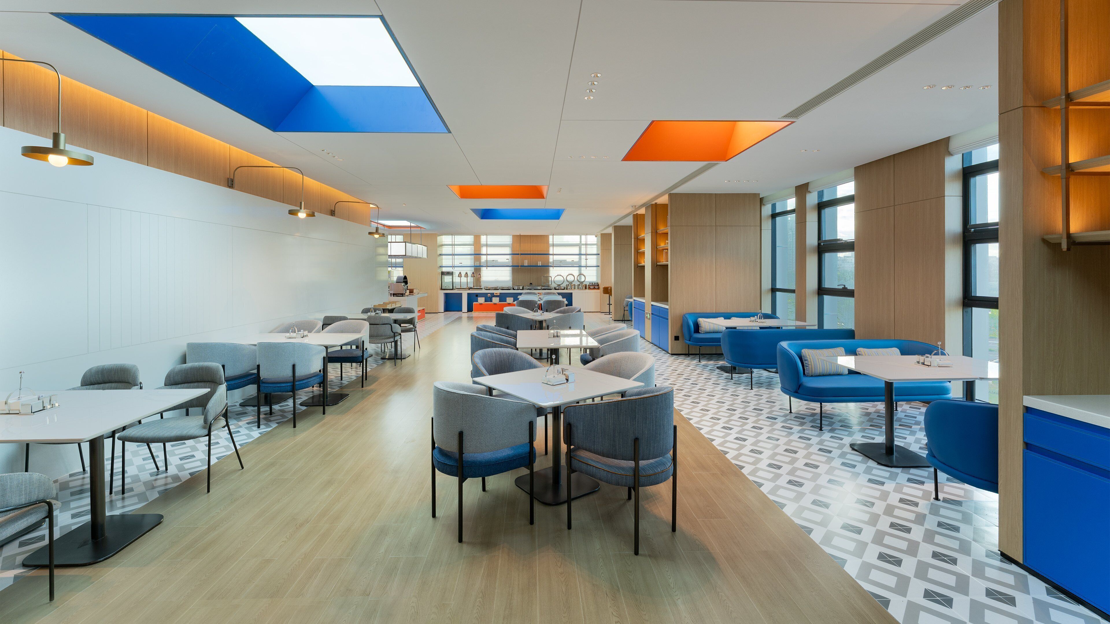 Uma sala de jantar moderna com pé direito alto, claraboias e diversos tipos de assentos, incluindo mesas e sofás.