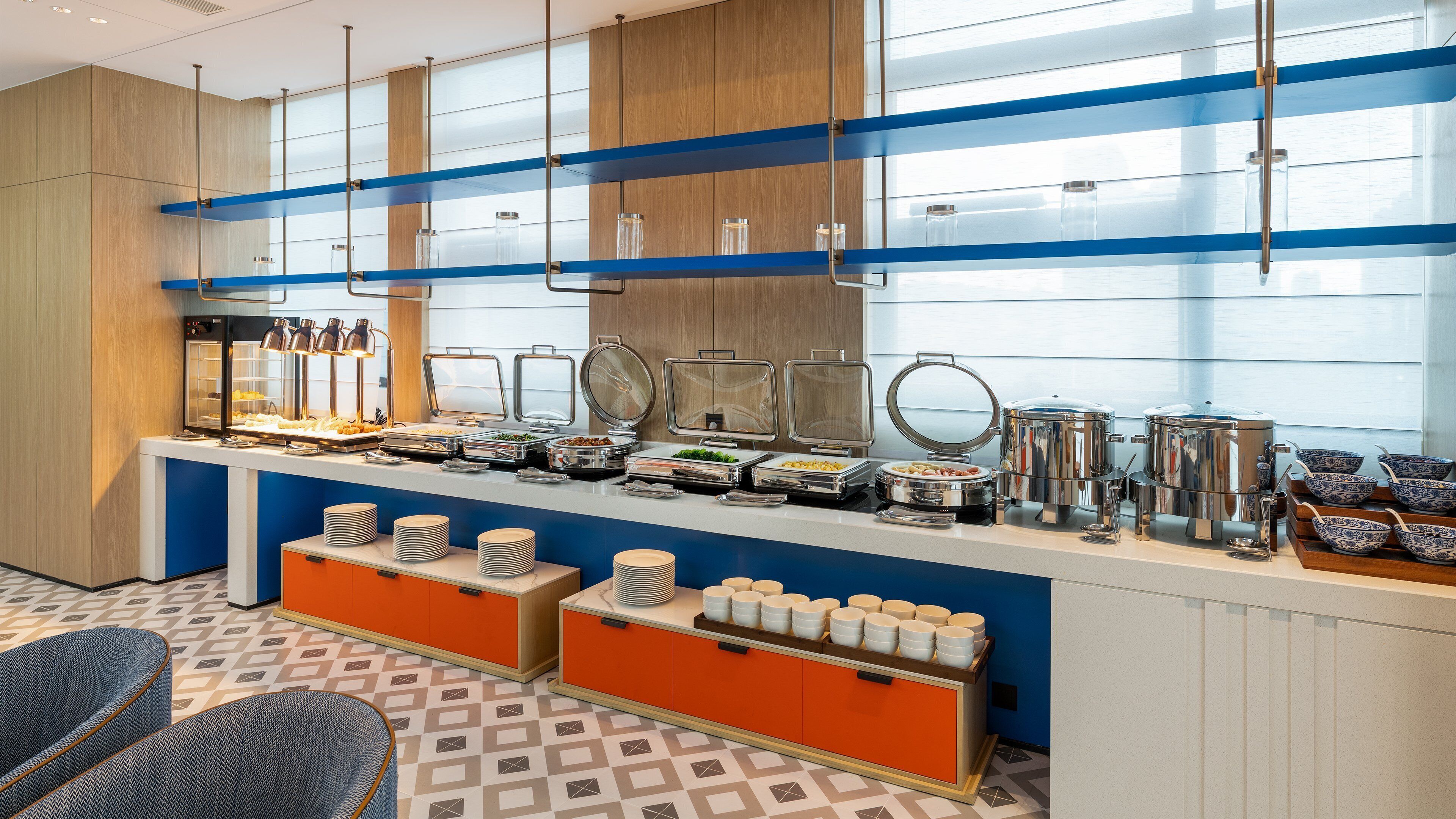 A buffet setup with various food containers and serving utensils, a coffee station, and seating area with chairs.