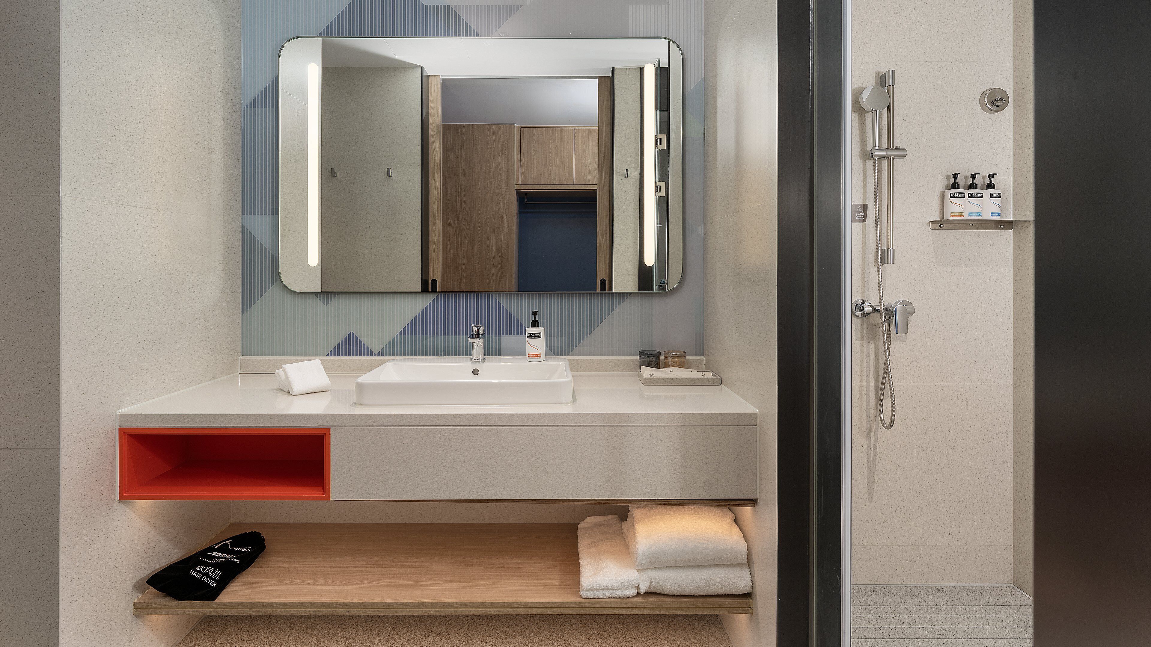 Une salle de bain moderne avec un grand miroir, un lavabo et une douche. On trouve des articles de toilette sur le lavabo et un porte-serviettes.