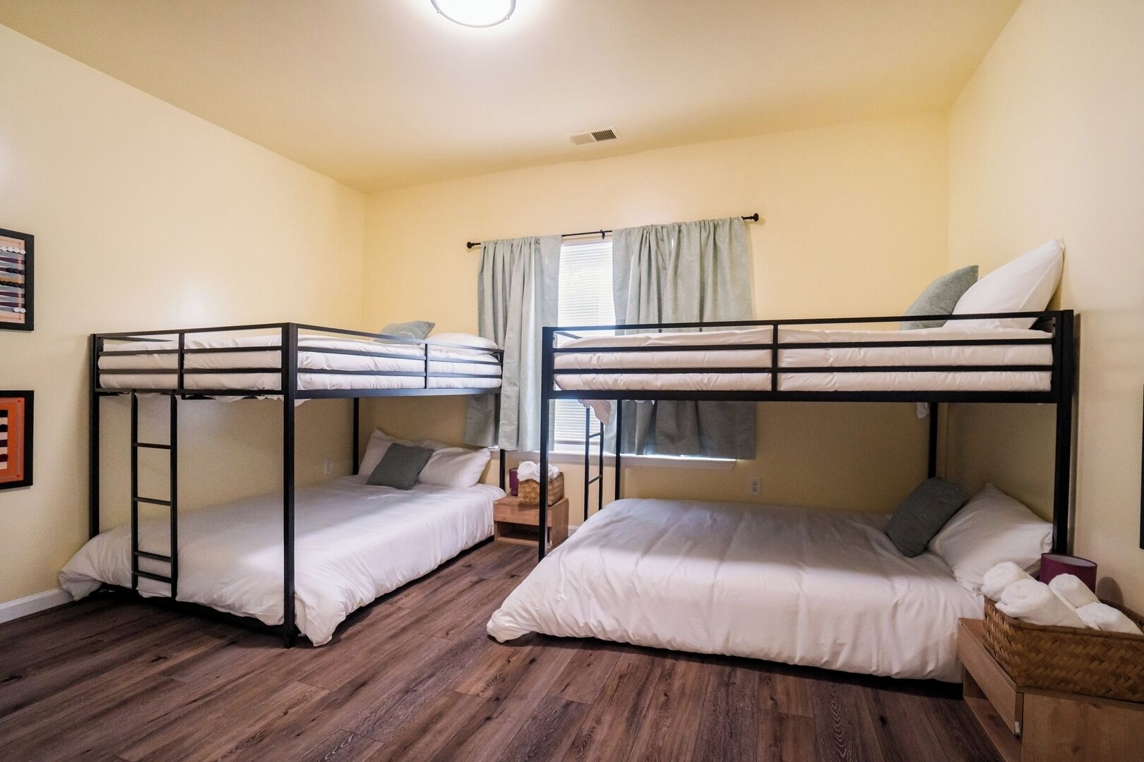 Una habitación con dos literas, suelo de madera, una ventana con cortinas y una mesita de noche de madera.