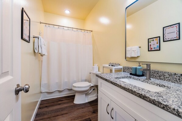 A bathroom with a toilet, shower curtain, sink, and a mirror.