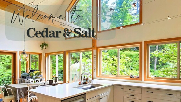 A modern kitchen with large windows, a central island, and a welcoming sign. - Cedar & Salt – Forest Retreat by the Beach with Hot Tub, Sauna & EV Charger (Tofino)