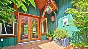 A wooden deck with a sliding glass door entrance, potted plants, and a mailbox. - Cedar & Salt – Forest Retreat by the Beach with Hot Tub, Sauna & EV Charger (Tofino)