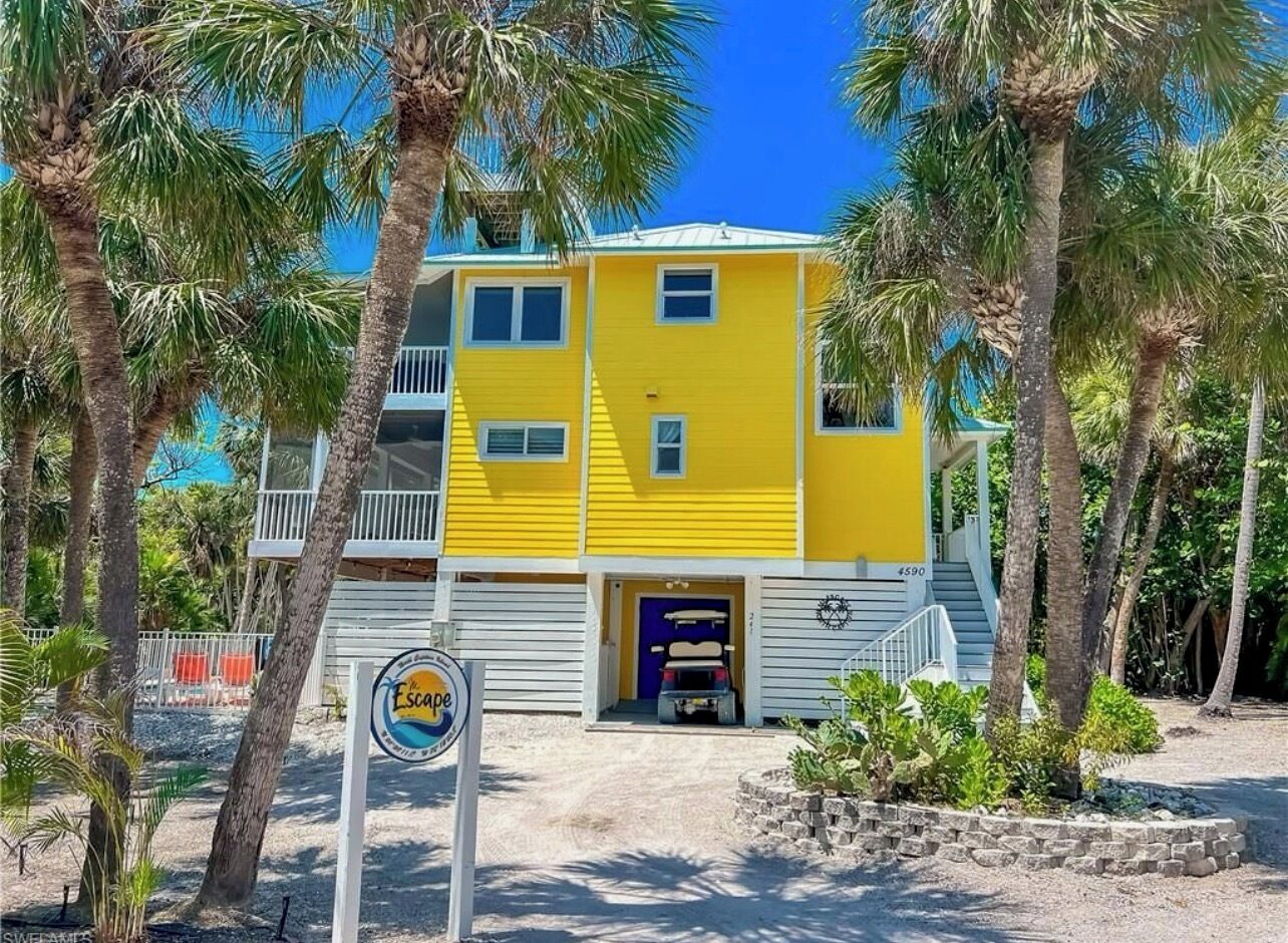 Un bâtiment jaune avec une porte bleue, entouré de palmiers et d’une enseigne sur laquelle on peut lire « Évasion ».