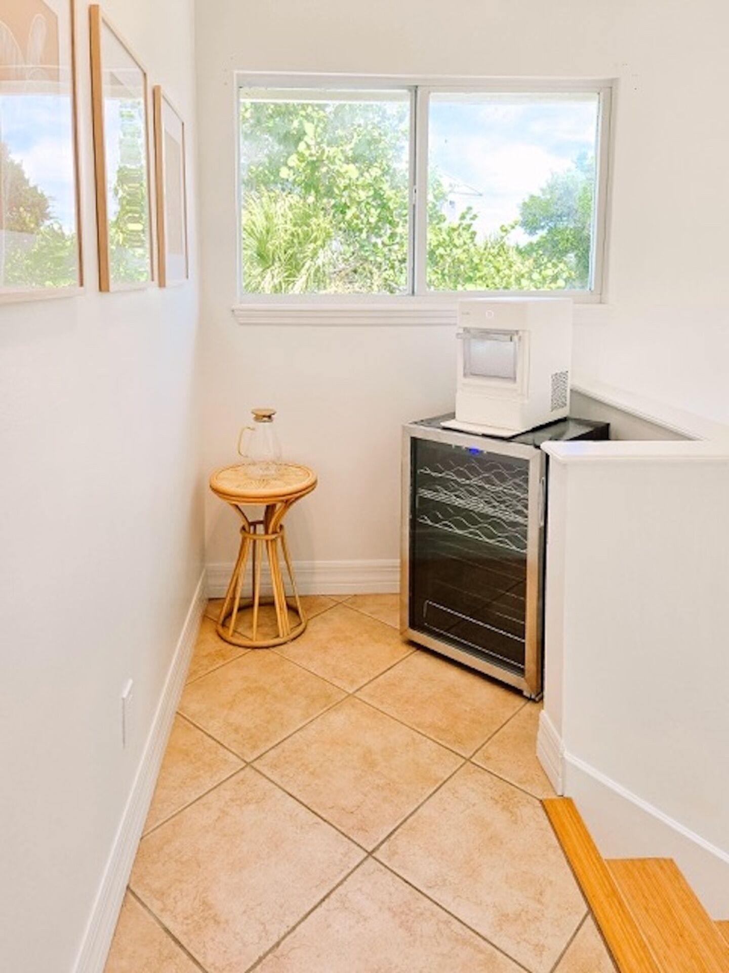 A small kitchen with a window, a microwave, a small table with a glass container, and a refrigerator.