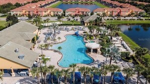 Un complejo turístico con una piscina grande, varias edificaciones con tejados rojos y una masa de agua al fondo.