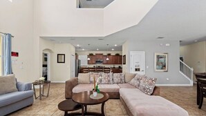 Amplia sala de estar con sofá, mesa de centro y mesa de comedor. Se ve una cocina al fondo.