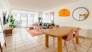A spacious living room with a large wooden dining table, comfortable seating, and a balcony with a view. - Beach Oasis w/ Balcony, Pool, Gym - Elevator to Beach (Miami Beach)