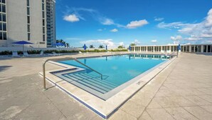 A rectangular pool with a tiled edge, surrounded by a paved area with lounge chairs and umbrellas. - Beach Oasis w/ Balcony, Pool, Gym - Elevator to Beach (Miami Beach)