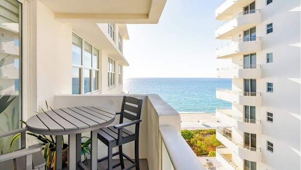 A balcony with a table and chairs, overlooking a beach and a sea view. - Beach Oasis w/ Balcony, Pool, Gym - Elevator to Beach (Miami Beach)