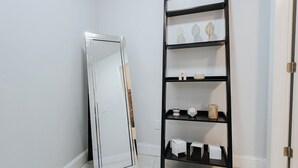 Un coin avec une porte blanche, une étagère noire ornée d’objets décoratifs et un miroir appuyé contre le mur.