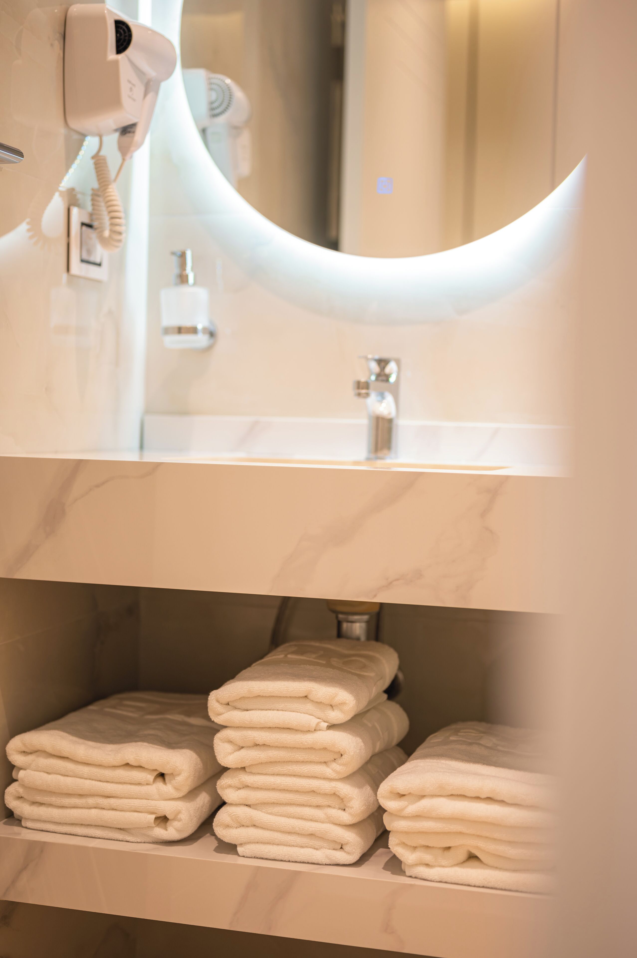 Un baño con espejo, secador de pelo y una pila de toallas.