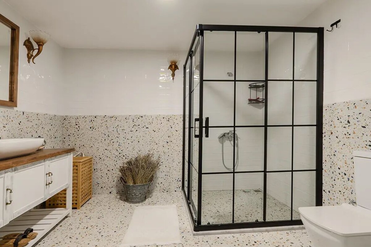 Um banheiro com chuveiro em box de vidro, pia branca e vaso sanitário branco.