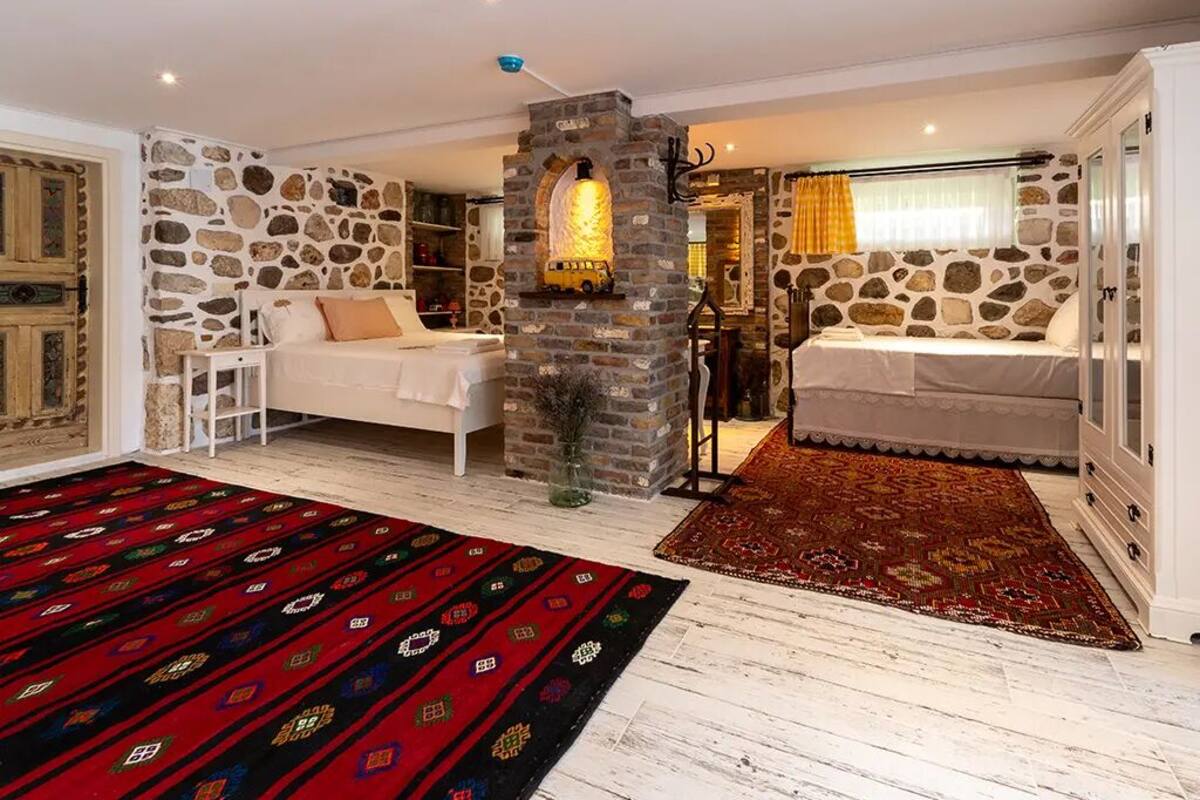 Une chambre avec un mur en pierre, un lit à baldaquin blanc, un tapis rouge à motifs et une cheminée en pierre.
