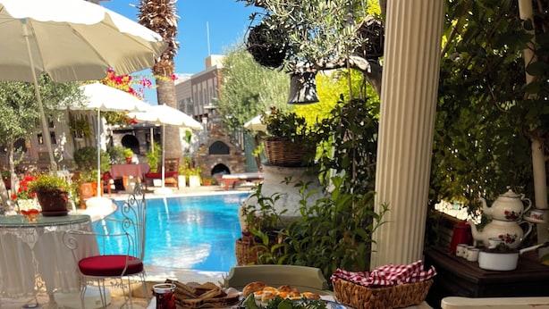 Ein Esszimmer mit gedecktem Tisch, verschiedenen Speisen und Getränken, umgeben von Sitzgelegenheiten im Freien und einem Pool im Hintergrund.