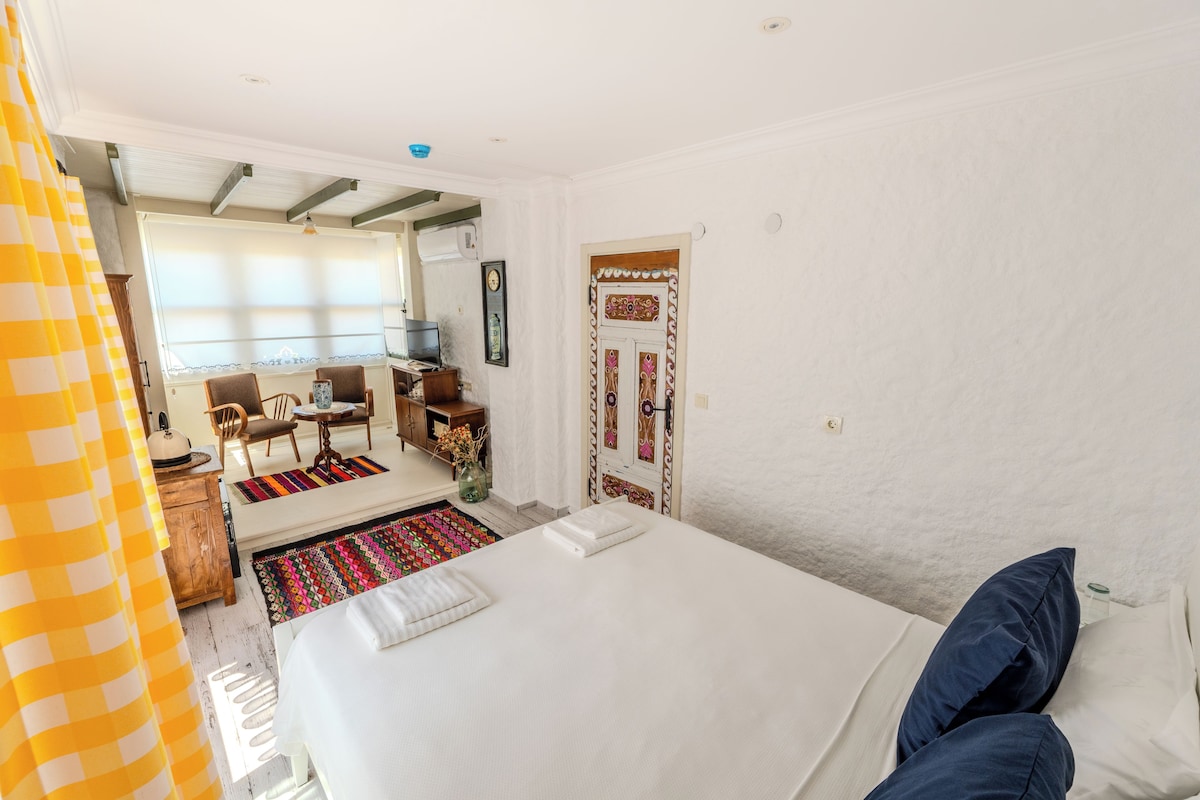 Quarto com uma cama grande, uma escrivaninha de madeira, uma cadeira e uma janela com persianas.