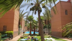 A courtyard with palm trees, a pool, and lounge chairs.
