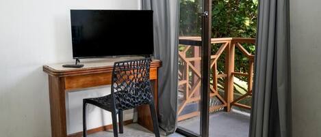 A room with a wooden desk, a black chair, a television, and a sliding glass door leading to an outdoor area with a wooden deck.