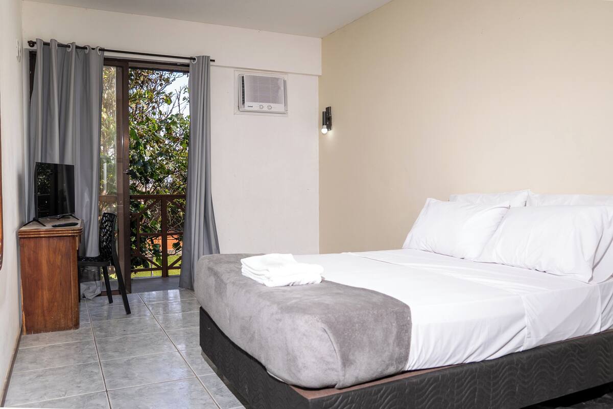 A bedroom with a bed, a desk, a chair, and a sliding glass door leading to an outdoor area.