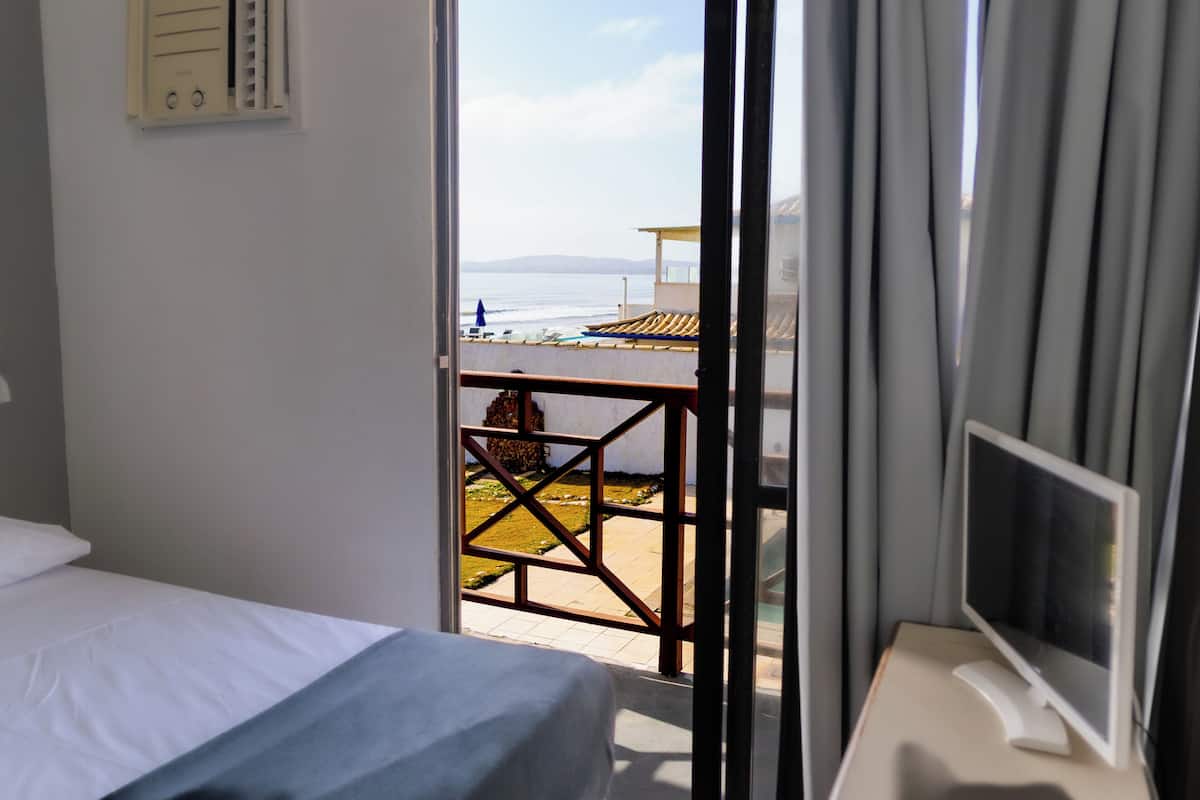A hotel room with a bed, a TV, and a balcony with a view of the sea.