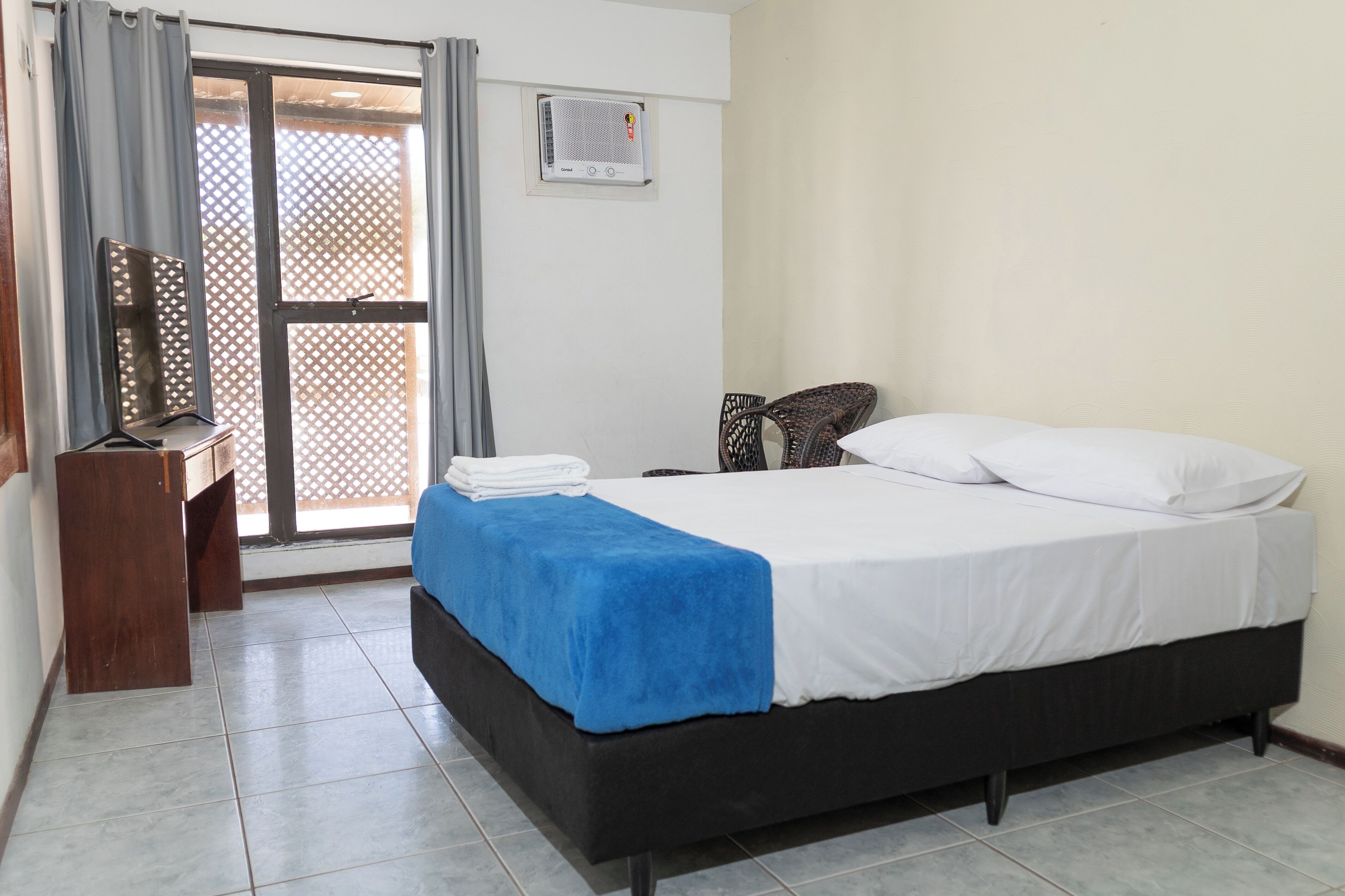 Un dormitorio con cama, escritorio y silla. Hay una ventana con cortinas y aire acondicionado instalado en la pared.