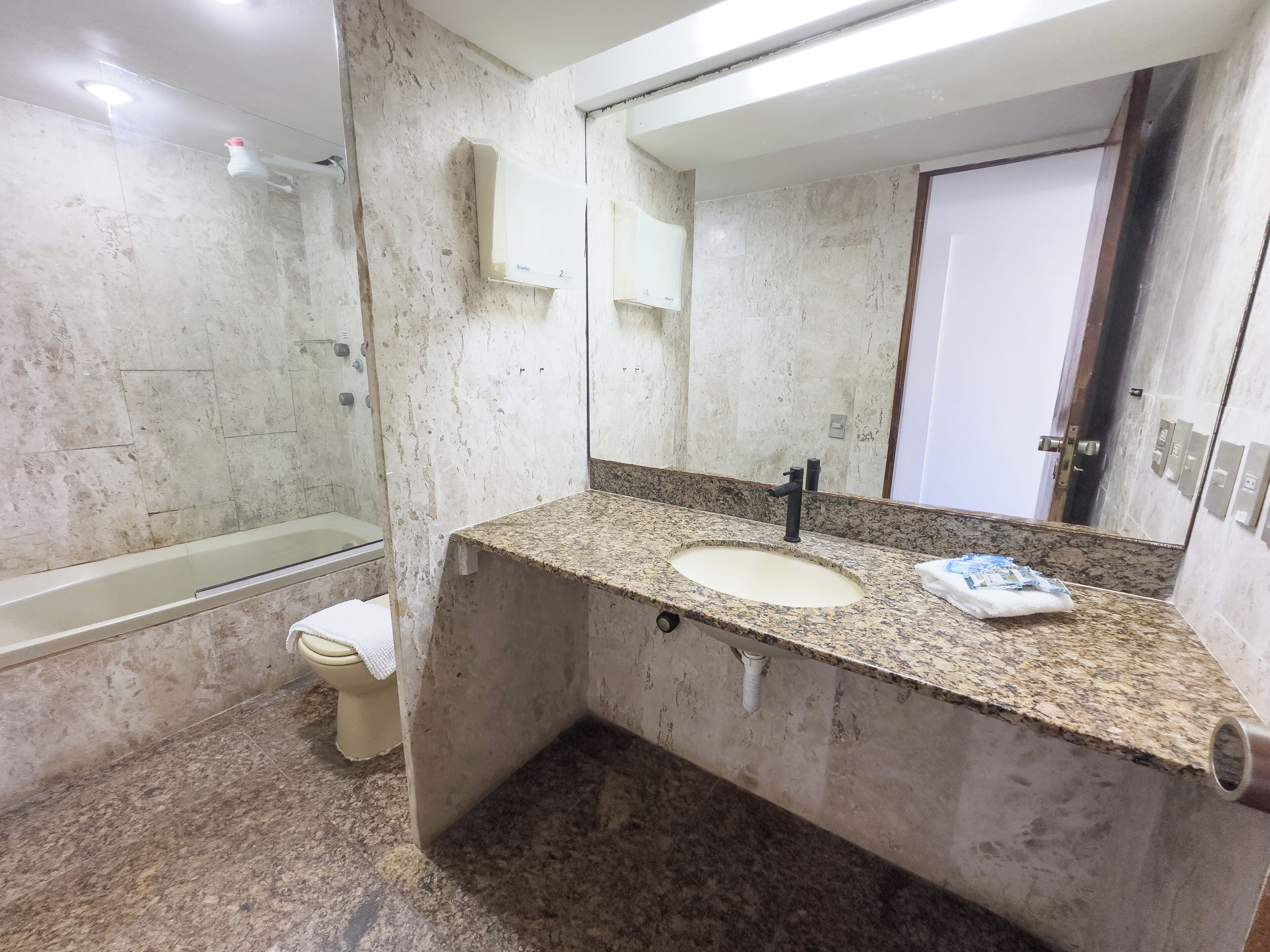 A bathroom with a granite countertop sink, a mirror, a toilet, and a bathtub.