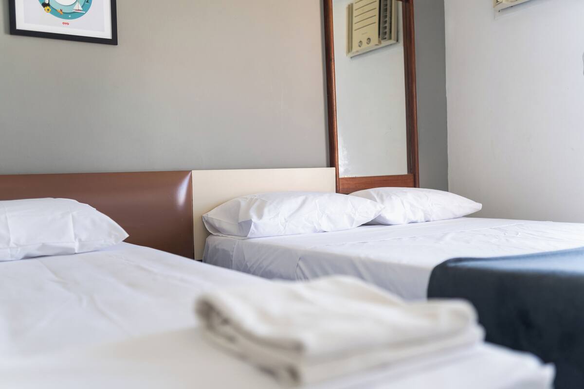 A hotel room with two beds, white linens, a wooden headboard, and a framed picture on the wall.