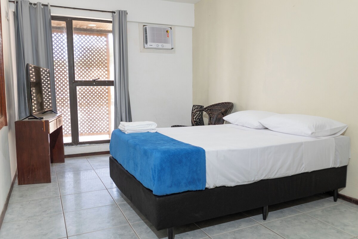 Un dormitorio con cama, escritorio y silla. Hay una ventana con cortinas y aire acondicionado instalado en la pared.