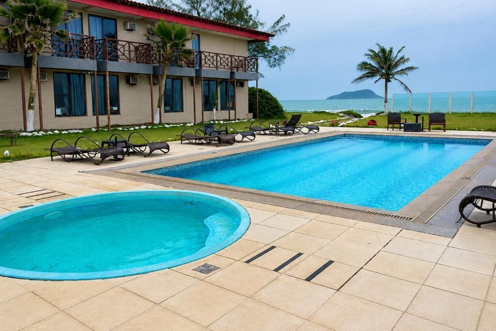 Una piscina con sillones de descanso, un edificio con balcones y vista al océano.