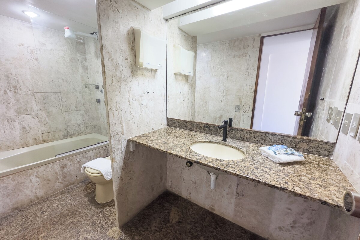 Un baño con lavamanos de encimera de granito, espejo, inodoro y bañera.
