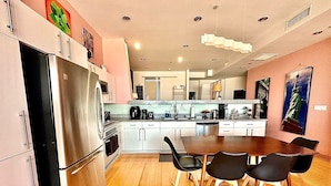 A modern kitchen with stainless steel appliances, a dining area with a wooden table and black chairs, and a painting of the Statue of Liberty on the wall.