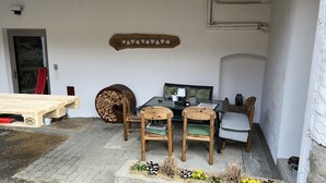 A wooden table and chairs set up on a paved patio with a white wall in the background. - Wandlhof vacation apartment (Niederösterreich)