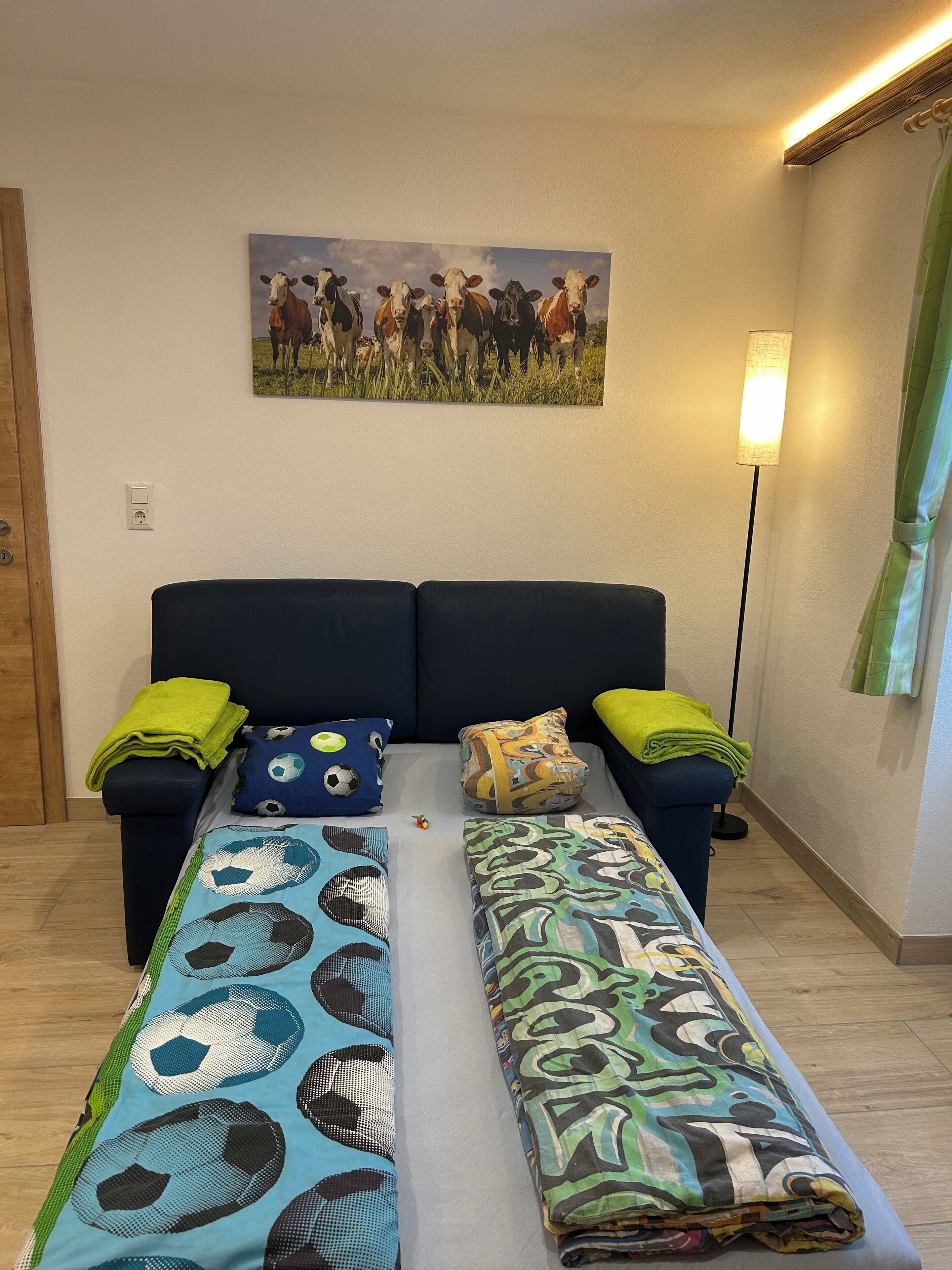 Une pièce comprenant un canapé-lit, deux oreillers, une couverture, une lampe et un tableau représentant des vaches.