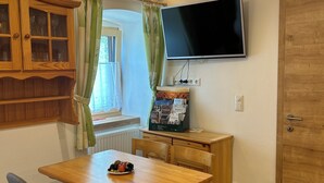 A cozy room with a wooden dining table, two chairs, a television mounted on the wall, and a wooden cabinet with glass doors. - Wandlhof vacation apartment (Niederösterreich)