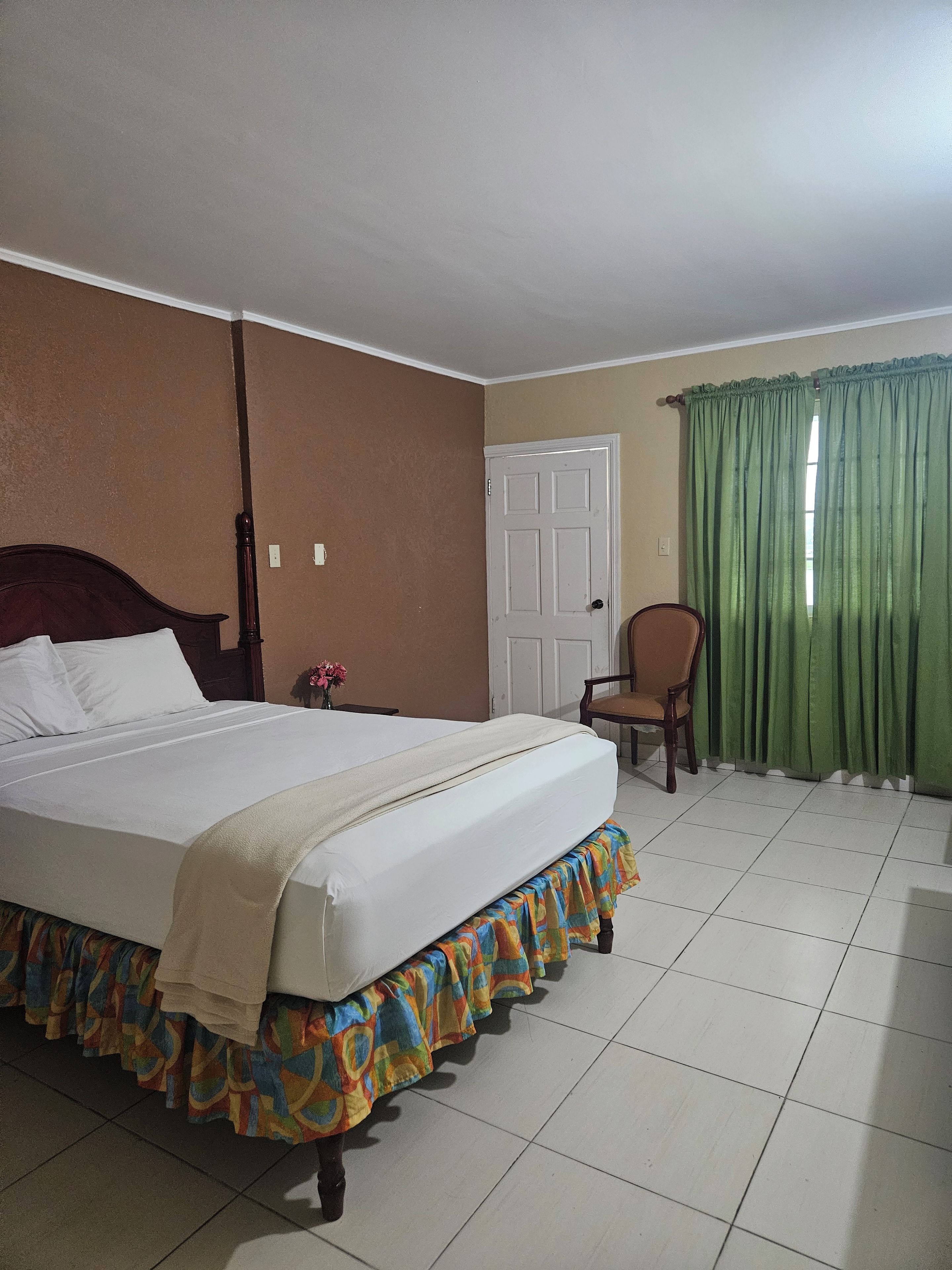 A hotel room with a bed, a chair, a door, and a window with curtains.