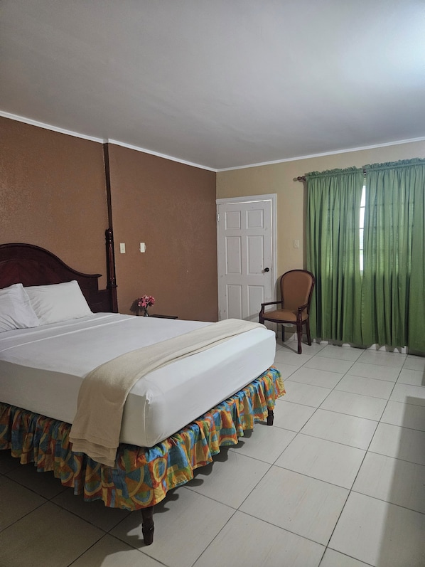 A hotel room with a bed, a chair, a door, and a window with curtains.