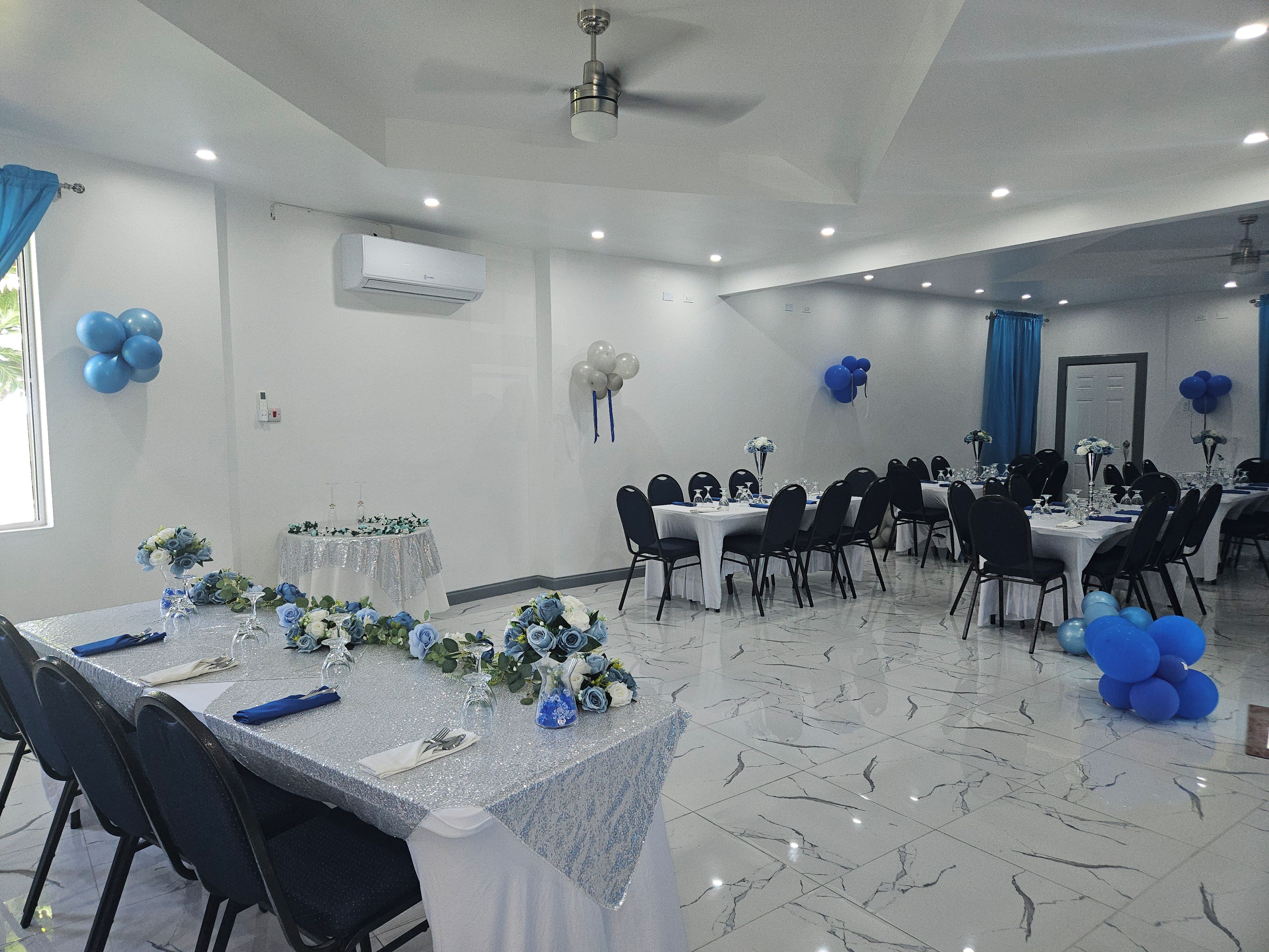 Un salón de banquetes con mesas dispuestas para un evento formal, con piso de mármol y ventiladores de techo.
