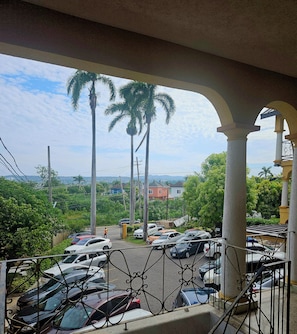 A parking area with multiple cars, a guard, and a view of a residential area with houses and palm trees.