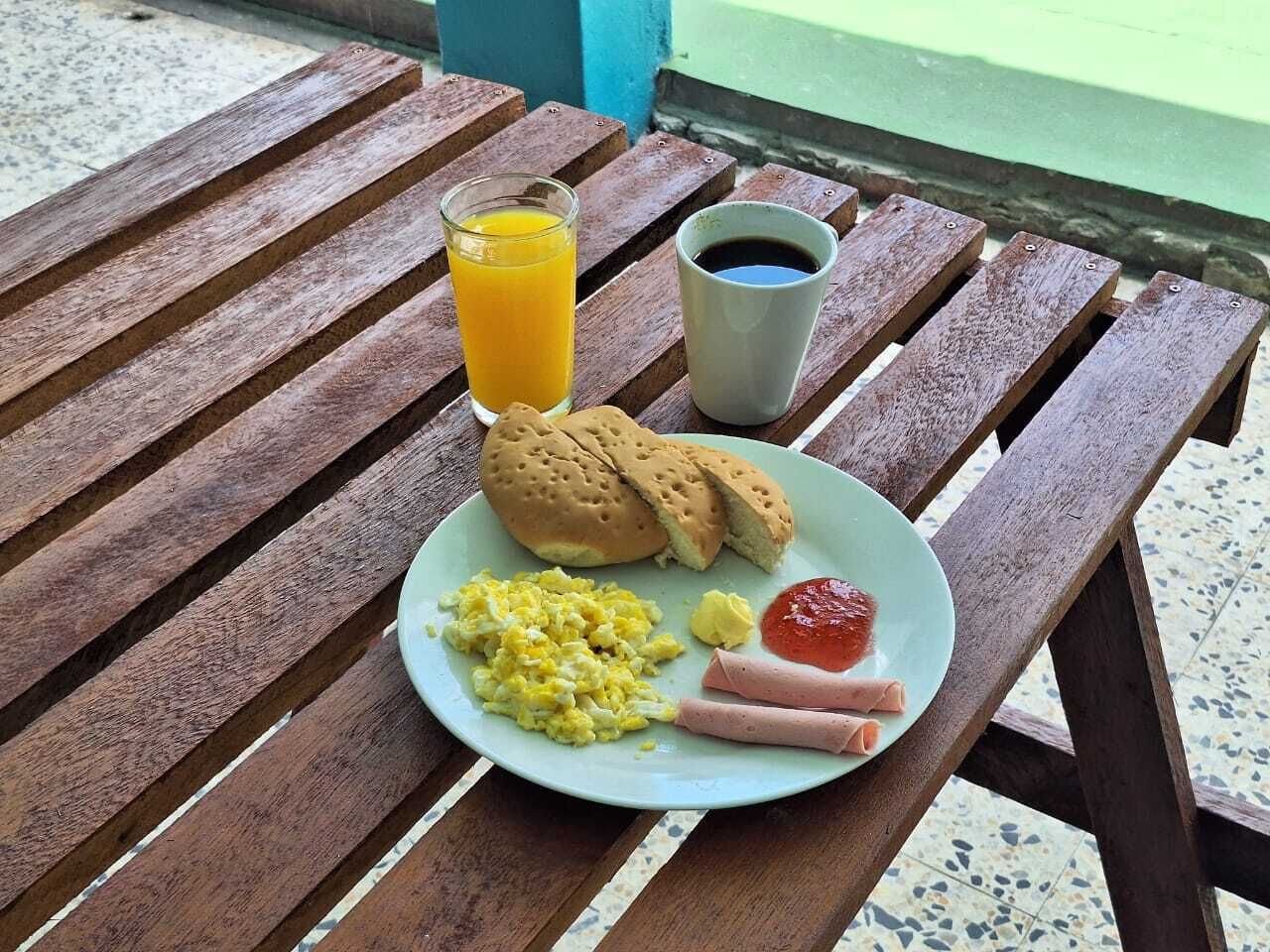 Une assiette contenant des œufs brouillés, des saucisses, du ketchup, un pain et un verre de jus d’orange, le tout posé sur une table en bois.