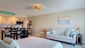 Ein gemütliches Wohnzimmer mit einer Couch, ein Essbereich mit Tisch und Stühlen, eine Küche mit Schränken und Geräten sowie ein Deckenventilator.