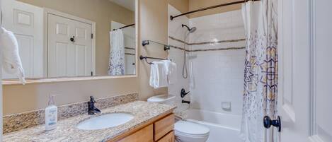 A bathroom with a granite countertop, white sink, and a shower with a patterned curtain.