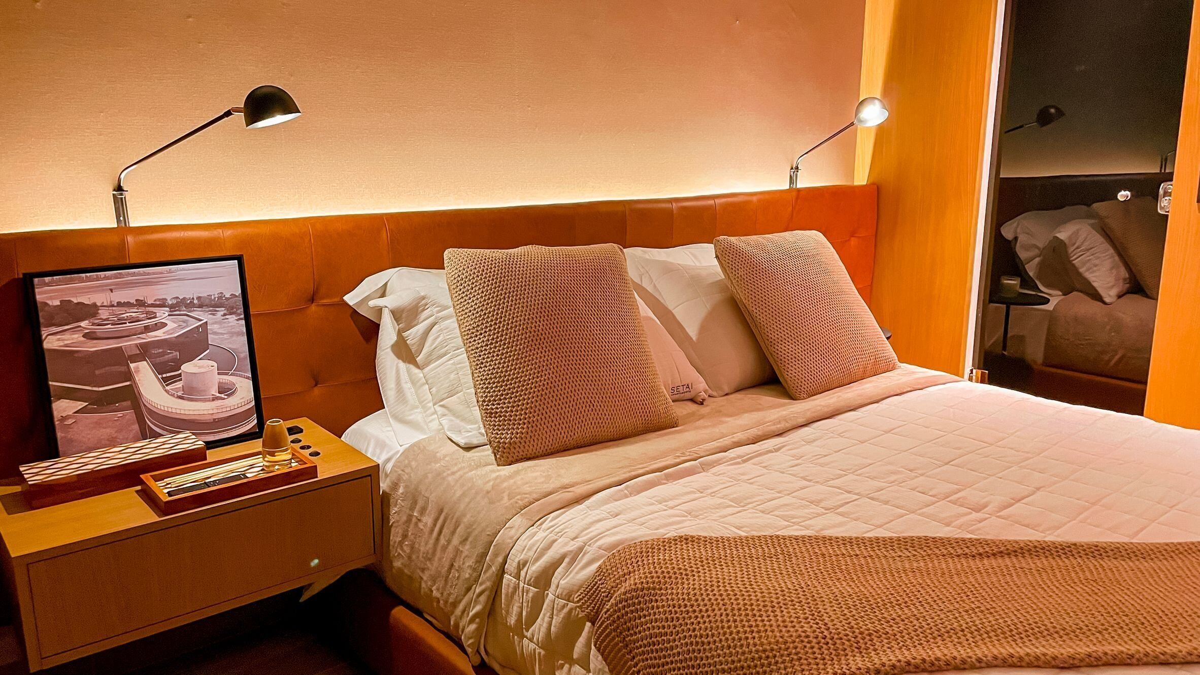 Ein Hotelzimmer mit Bett, Nachttisch mit Lampe, Fernseher und Blick auf die Stadt.
