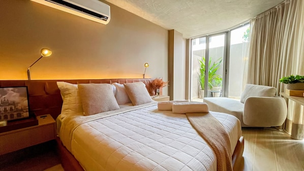 Een moderne hotelkamer met een groot bed, bedlampjes, een nachtkastje, een klein tafeltje met een plant en uitzicht op groen door het raam.